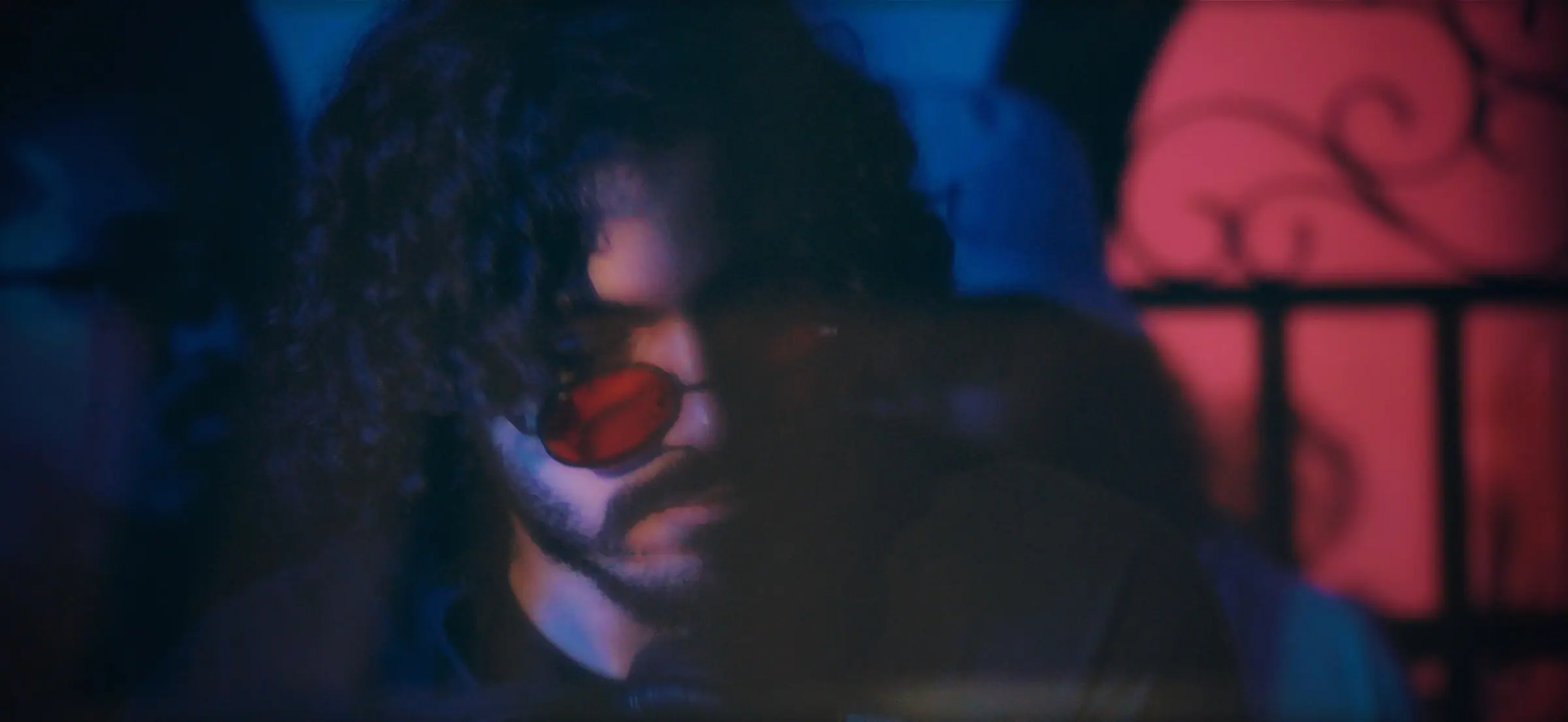 A film still of SOUL in red-lensed glasses, blue and red light