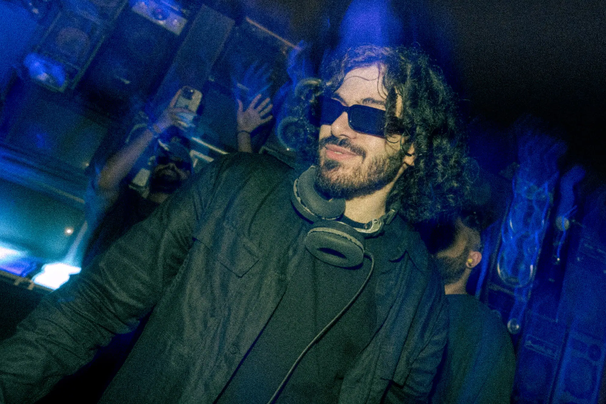 SOUL behind the booth in blue light, headphones around his neck, the crowd's hands raised behind him