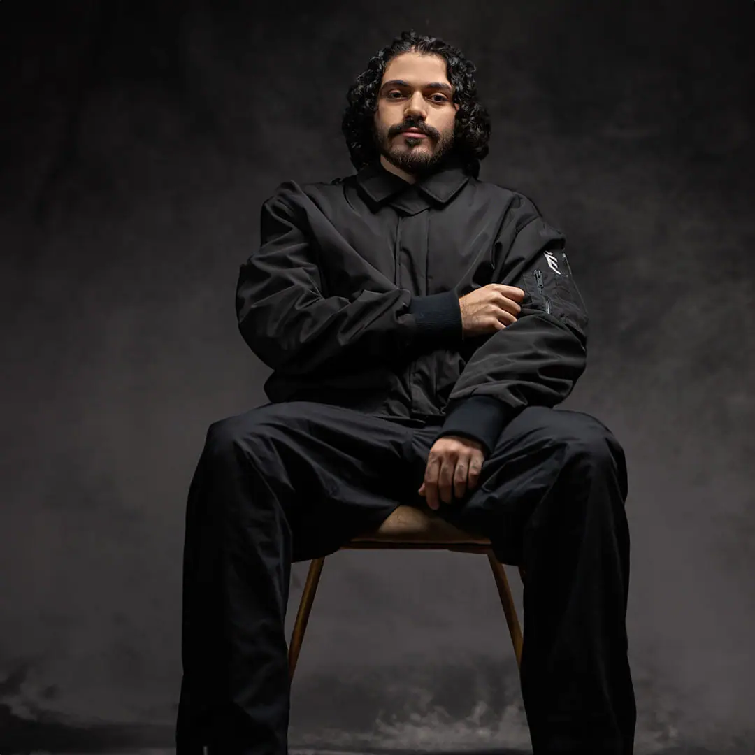 SOUL seated on a wooden chair in a smoky studio, in black