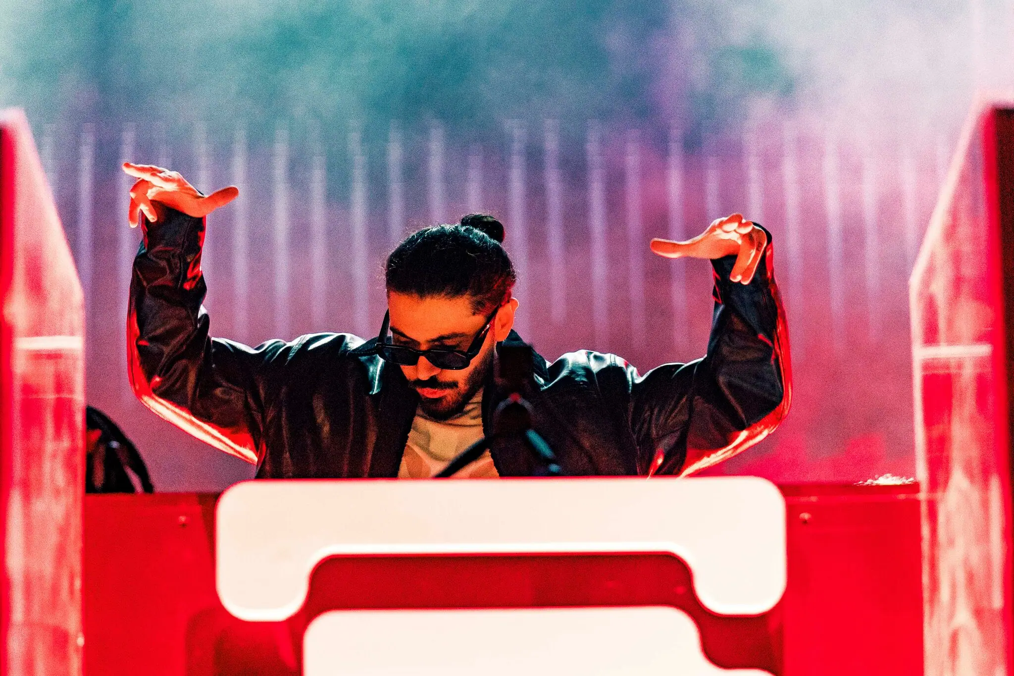 SOUL at the decks with both hands raised, red light and haze behind him